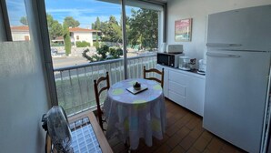 Un petit balcon avec une table et des chaises, un réfrigérateur et un four à micro-ondes.