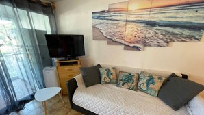 Une chambre à coucher avec un lit, une télévision, une petite table et un tableau représentant une scène de plage.