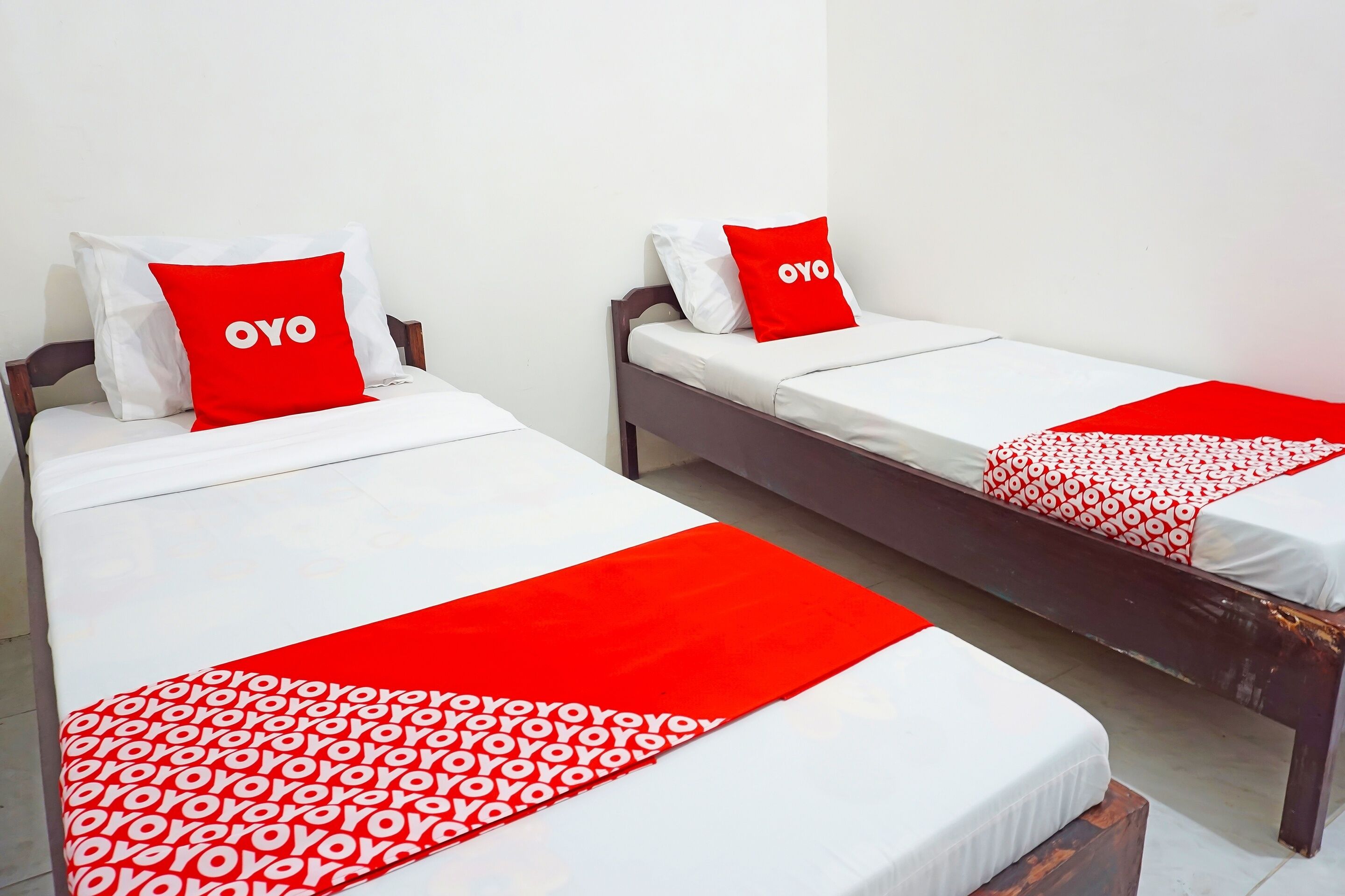 Dos camas individuales con ropa de cama blanca y roja, cada una con una almohada con el letrero "OYO".