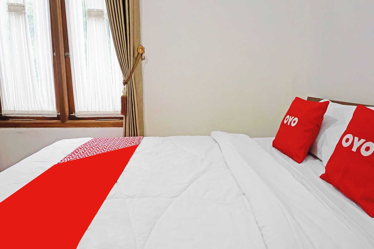 Un lit avec une literie blanche et des touches de rouge, une fenêtre avec des rideaux et un crochet fixé au mur.