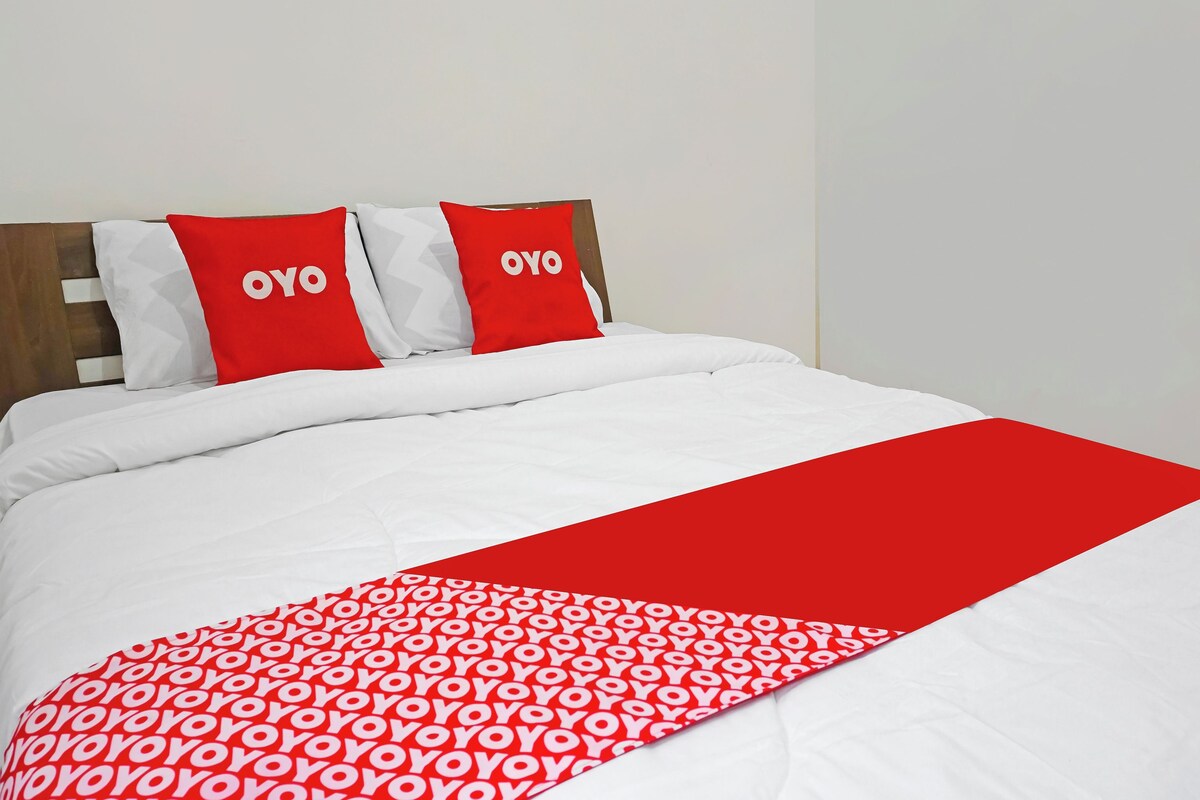 Een bed met witte beddengoed en twee rode kussens met 'OYO' tekst, een rode deken met een wit patroon, en een houten hoofdbord.