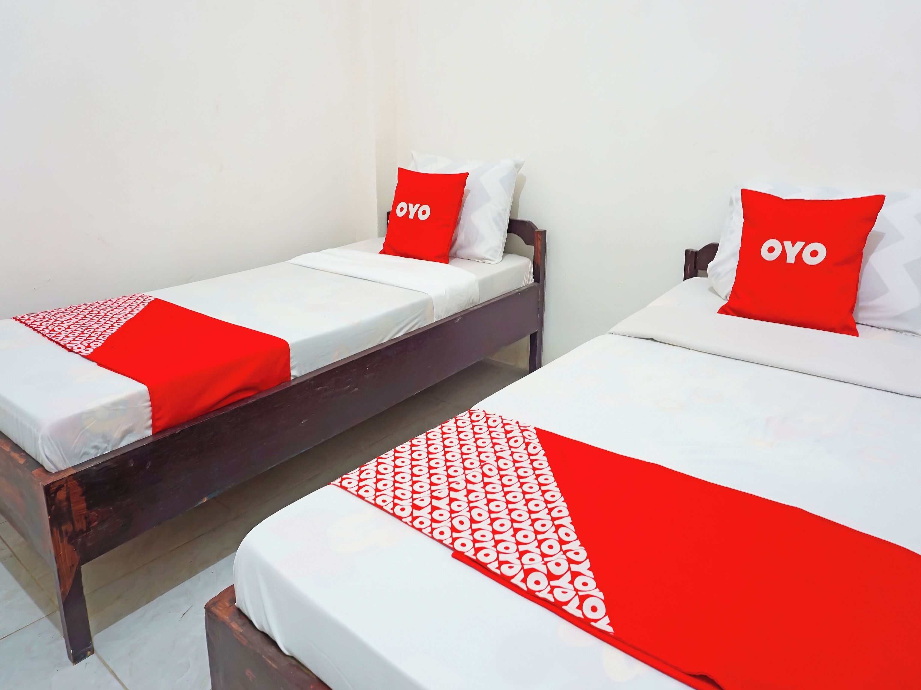 Dos camas individuales con cabeceros de madera, ropa de cama blanca y detalles en rojo, incluyendo almohadas y una colcha.