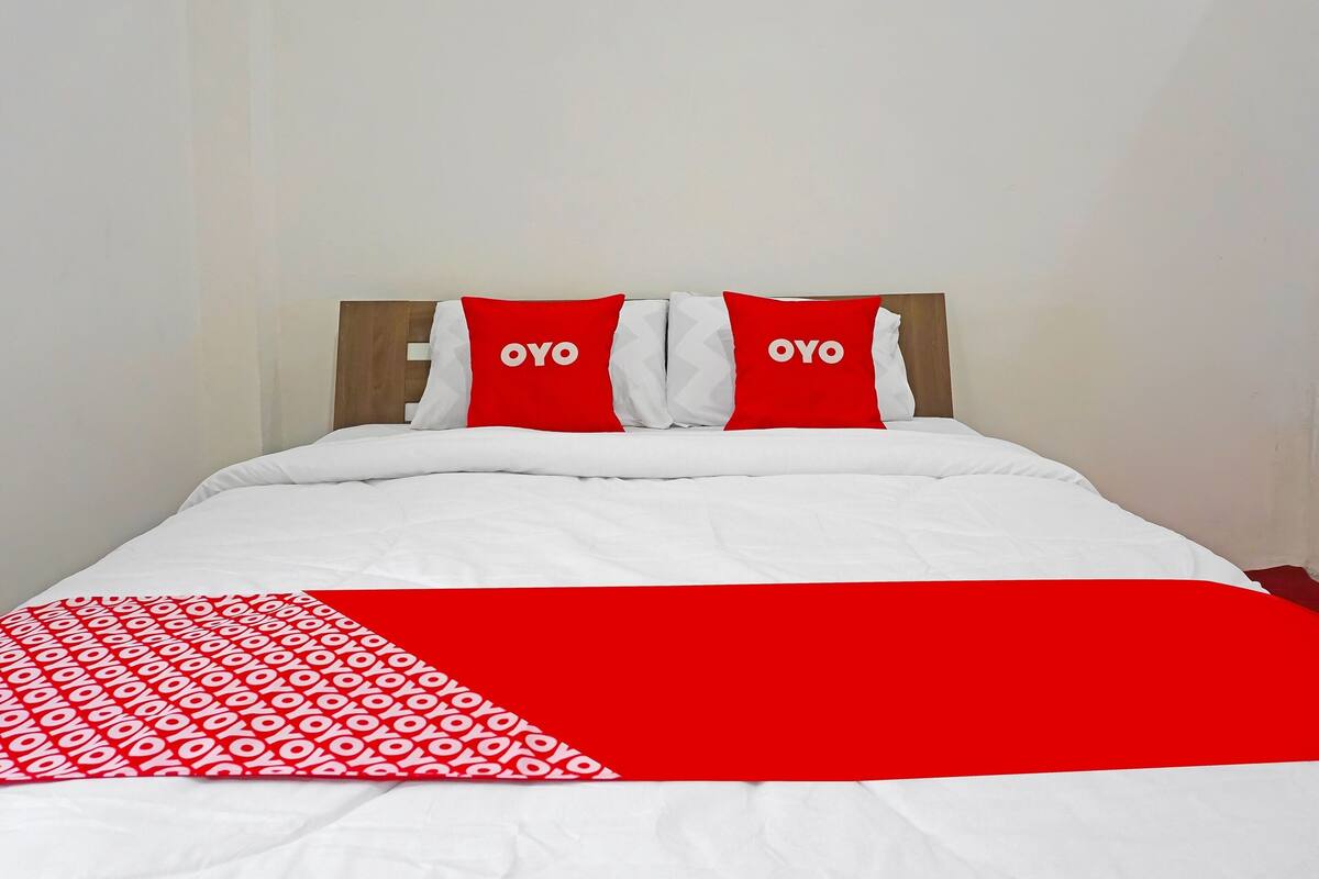 Een bed met wit beddengoed en twee rode kussens met de tekst 'OYO'.