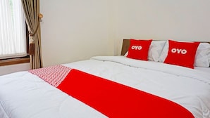 Een hotelkamer met een bed, twee kussens met 'OYO'-branding, een rode en witte dekbedovertrek en een raam met gordijnen.