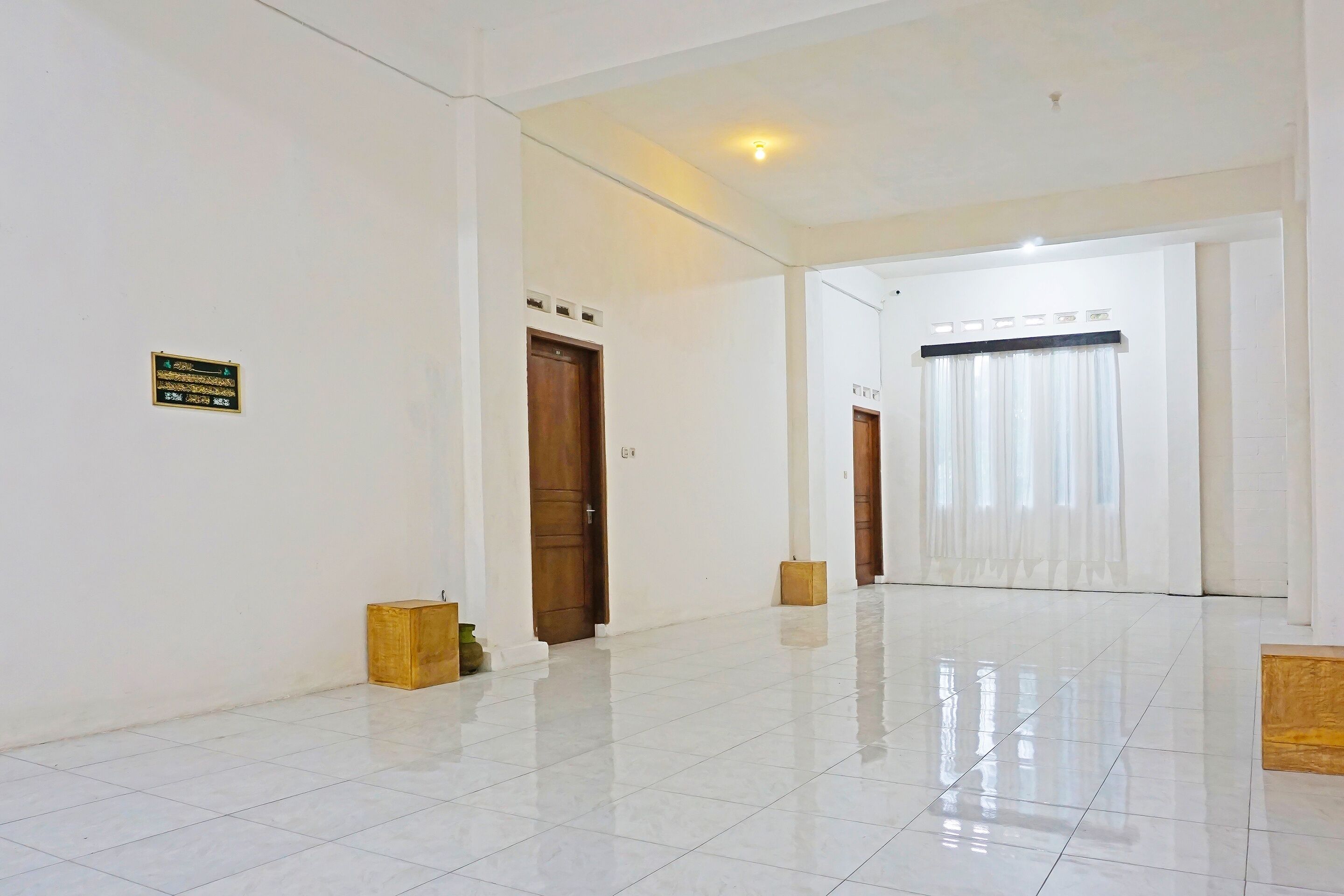 A spacious, well-lit hallway with white walls, a tiled floor, and a wooden door at the end.