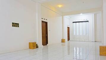 A spacious, well-lit hallway with white walls, a tiled floor, and a wooden door at the end.