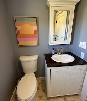 A bathroom with a toilet, sink, cabinet, and a framed artwork on the wall.