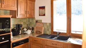 Een keuken met houten kastjes, een Bosch vaatwasser, een koffiezetapparaat en een raam met uitzicht op sneeuw.