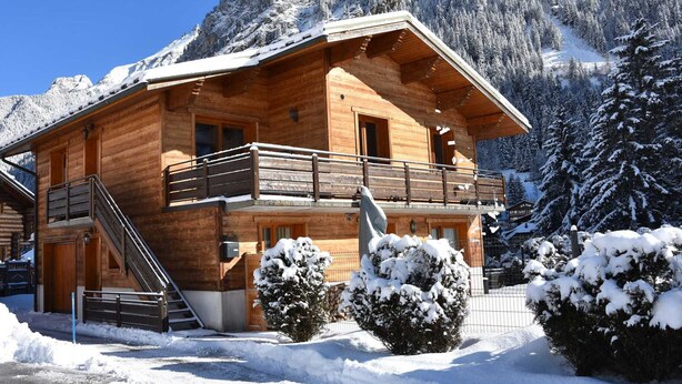 Een houten chalet met een balkon en een trap, omgeven door sneeuw.