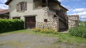Ein zweistöckiges Steinhaus mit einem Balkon, einer Holztür und einer Steintreppe, die zum Obergeschoss führt.