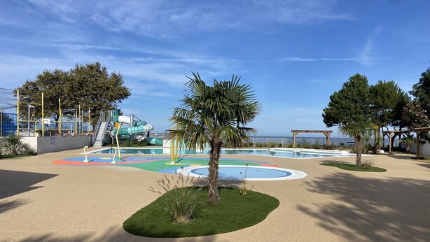 Un terrain de jeux avec un toboggan aquatique, des palmiers et une vue sur la mer.