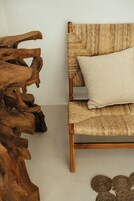 A wooden chair with a woven backrest and a cushion, placed against a plain wall.