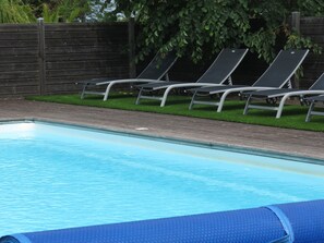 En swimmingpool med ett trädäck och en gräsyta med solstolar.