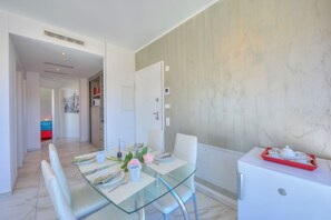 Un comedor moderno con una mesa de vidrio, sillas blancas y un refrigerador blanco.