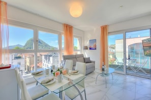 Una sala de estar moderna con una mesa de comedor de vidrio, sofás blancos y un balcón con mobiliario exterior.