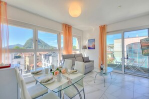 A modern living room with a glass dining table, white sofas, and a balcony with outdoor seating. - Attico al Parco: Penthouse in Lugano Balcony, A/C & 2 min From Lake (Lugano)