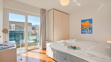 Camera d'albergo con letto, scrivania, sedia, armadio e balcone con vista sulla città.