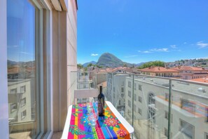 A balcony with a colorful tablecloth, a bottle, and a glass, overlooking a cityscape with buildings and a mountain. - Attico al Parco: Penthouse in Lugano Balcony, A/C & 2 min From Lake (Lugano)