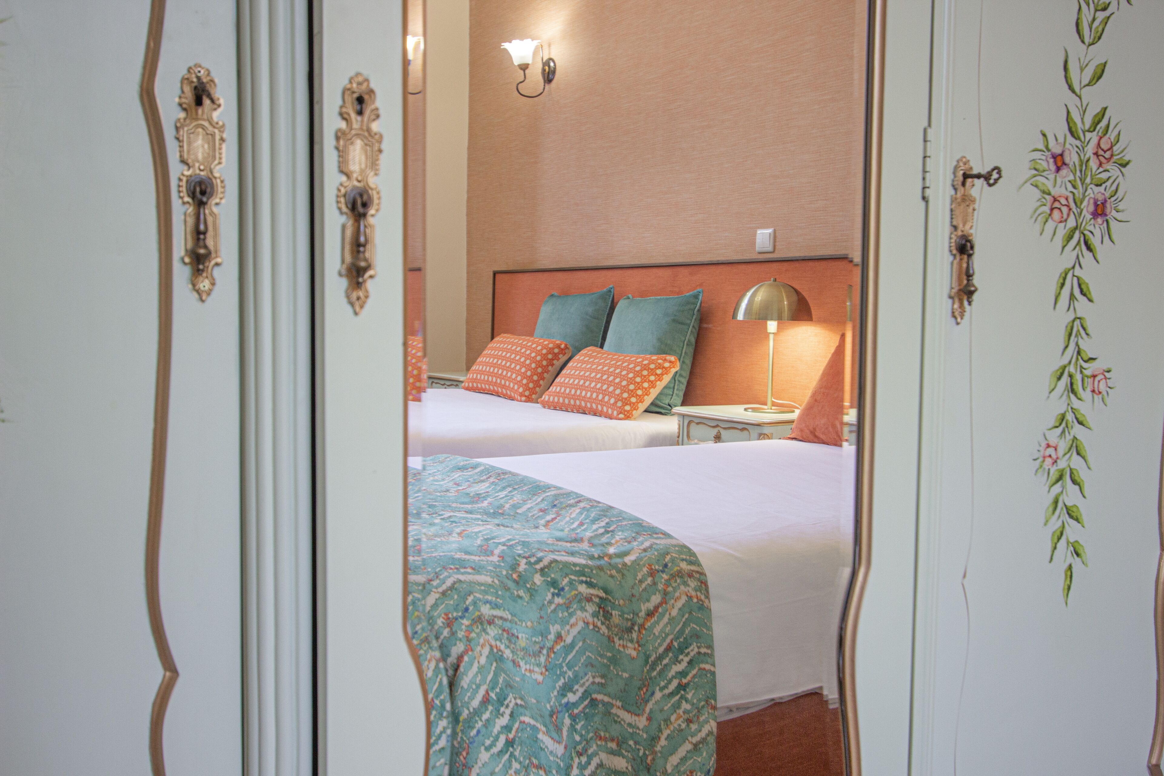 Une chambre d’hôtel avec deux lits, une table de chevet, une lampe et un luminaire fixé au mur.