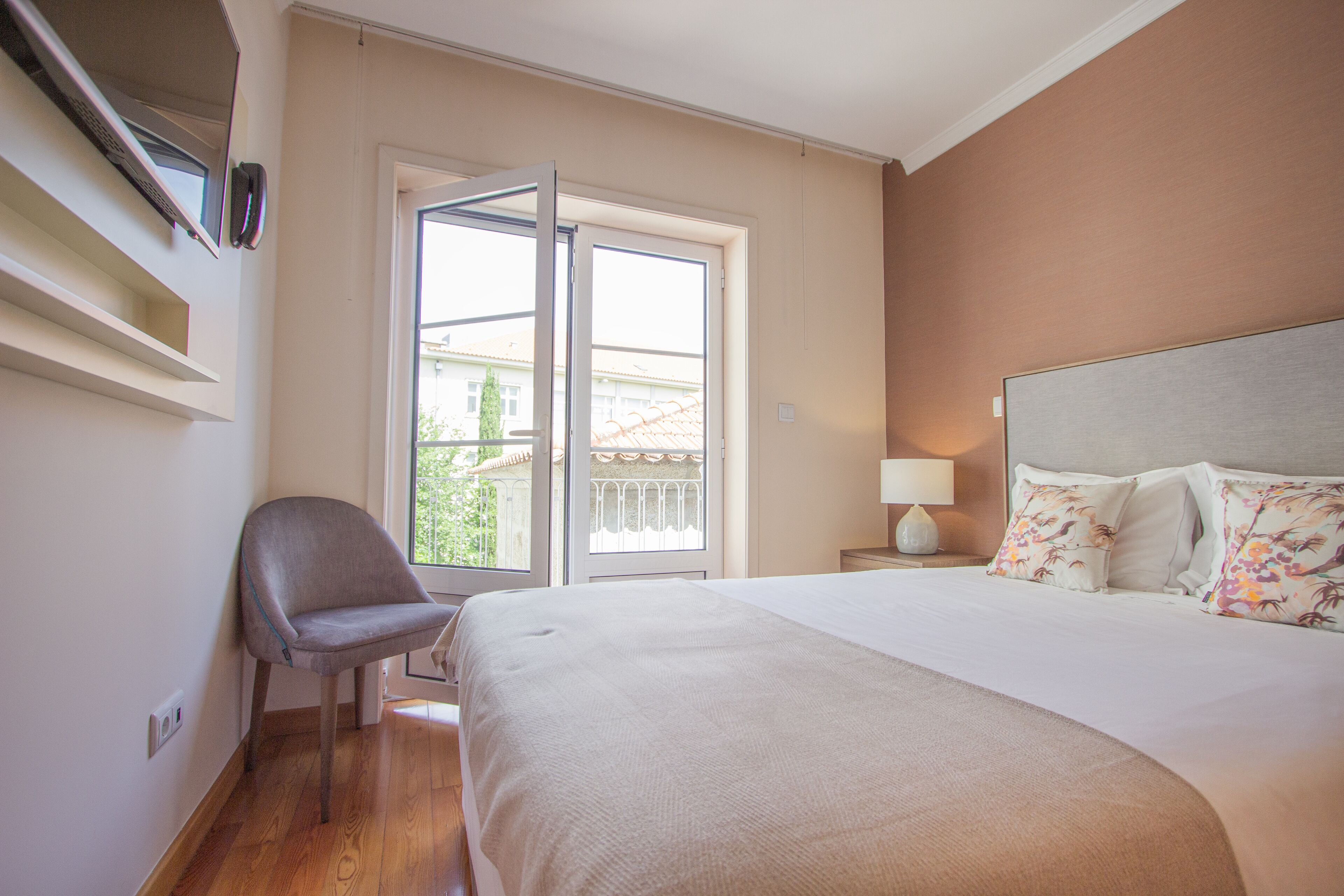 A hotel room with a bed, a chair, a window, and a nightstand with a lamp.