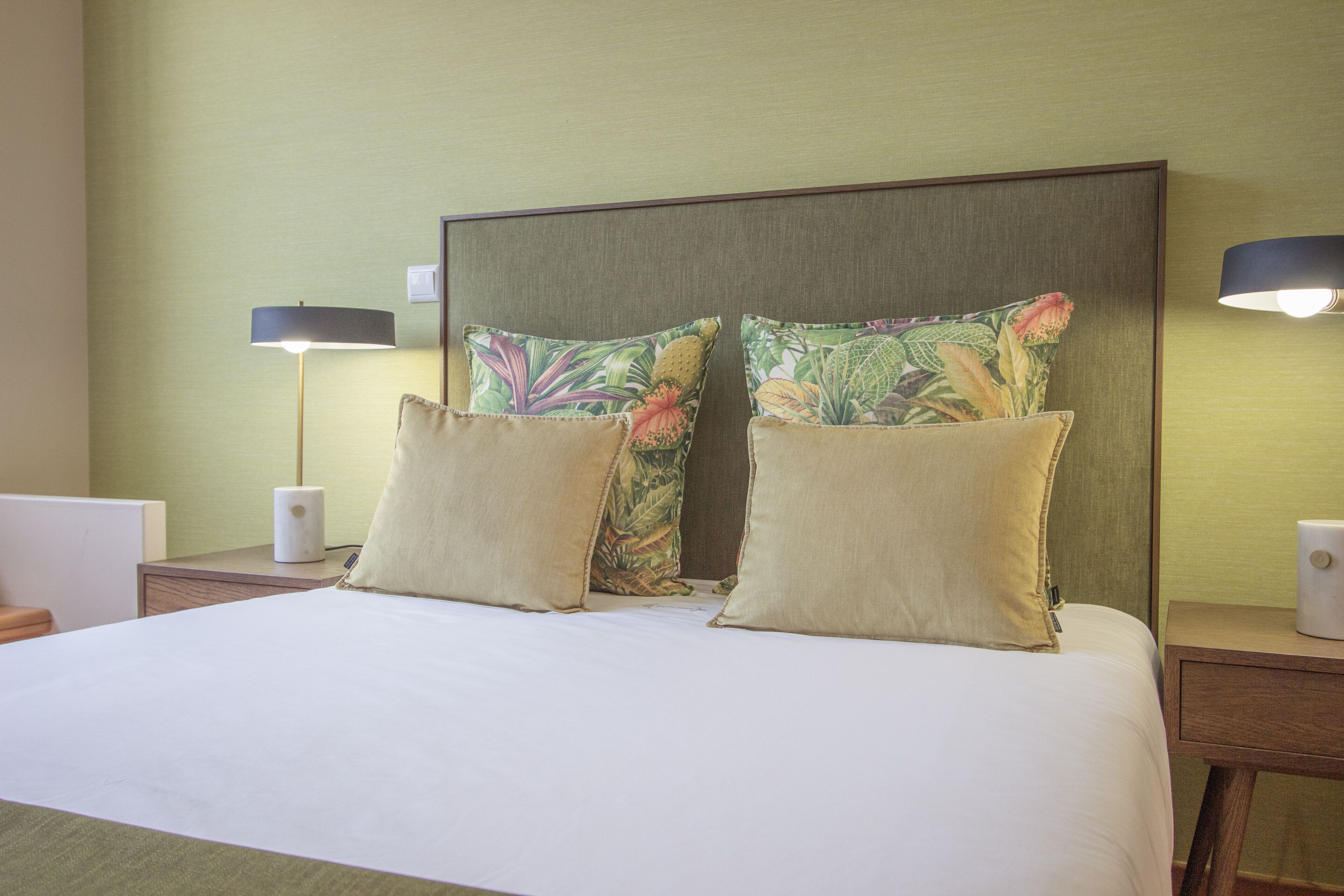 Habitació d'hotel amb un llit gran, dues làmpades de nit i un capçal amb coixins florals.