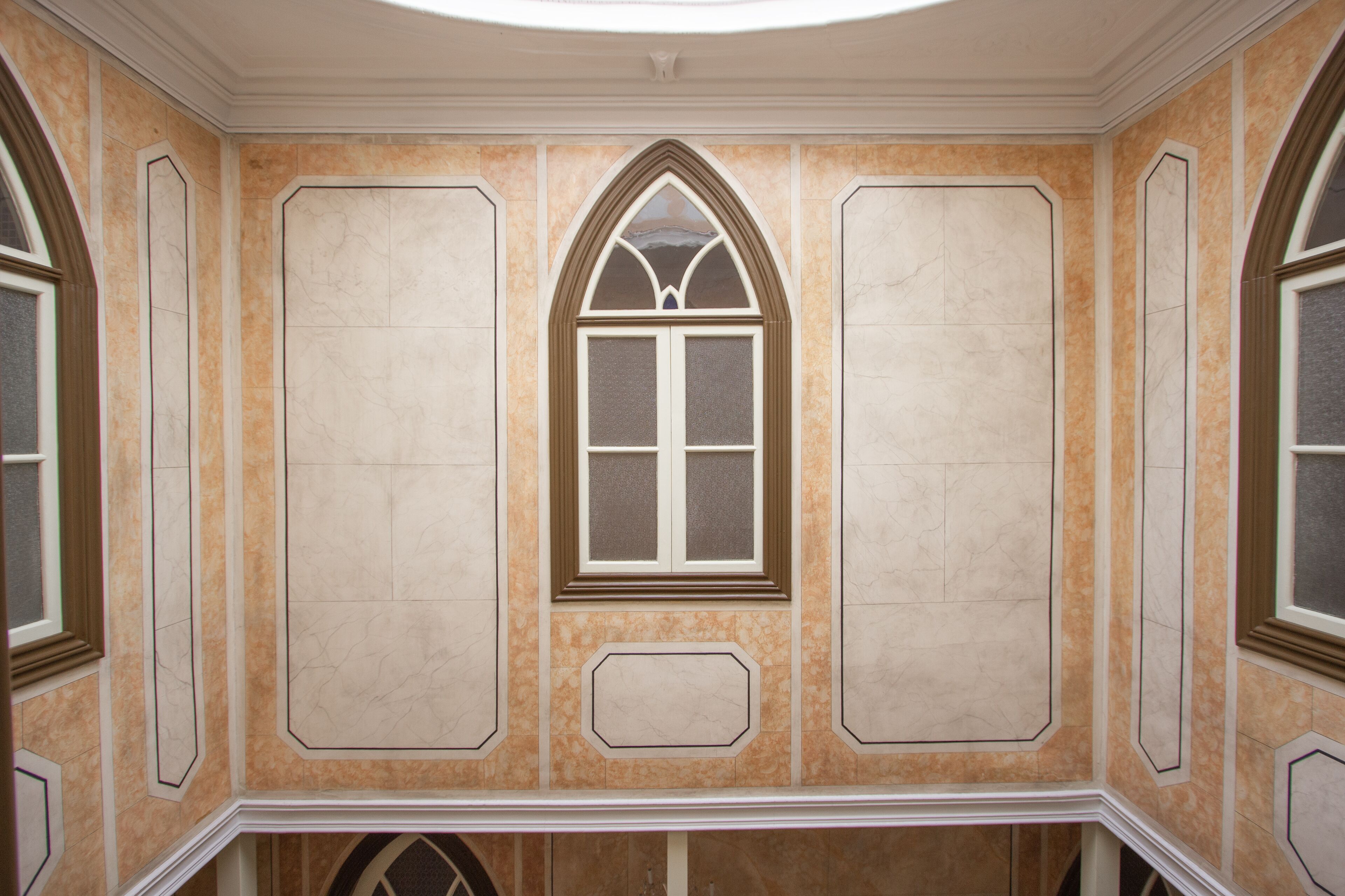 A room with a large arched window, decorative moldings, and a marble-like wall finish.