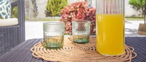 A wicker table with a woven placemat, two clear glasses, and a glass pitcher of yellow liquid.