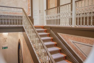 Una escalera con barandillas metálicas decorativas, peldaños alfombrados y una puerta al fondo.