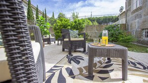 Un espace extérieur aménagé en terrasse, avec des meubles en osier, un sol à motifs et une table sur laquelle se trouvent une carafe en verre et un verre.