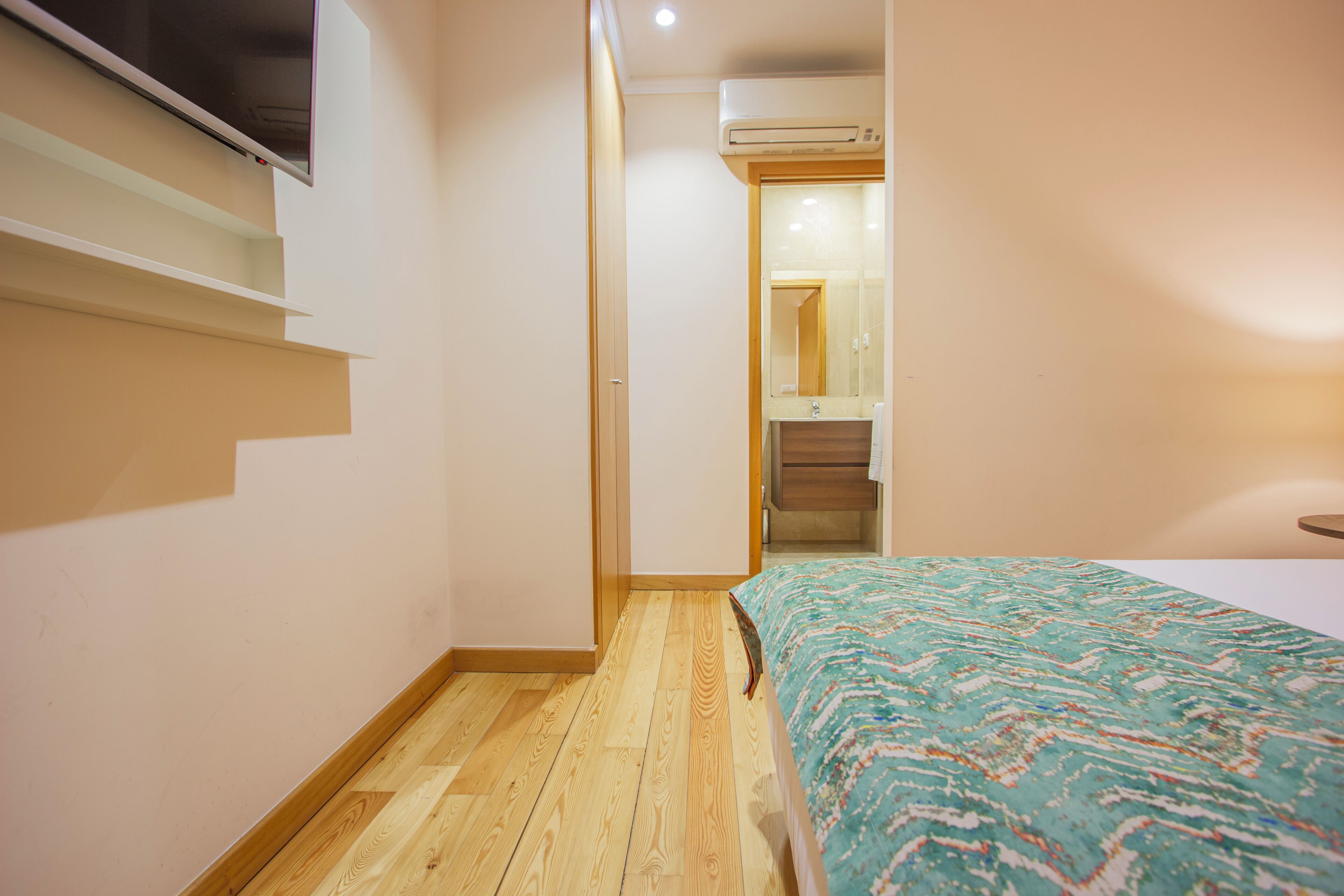 Een slaapkamer met een bed, een houten vloer, een inbouwkast en een deur naar een badkamer.