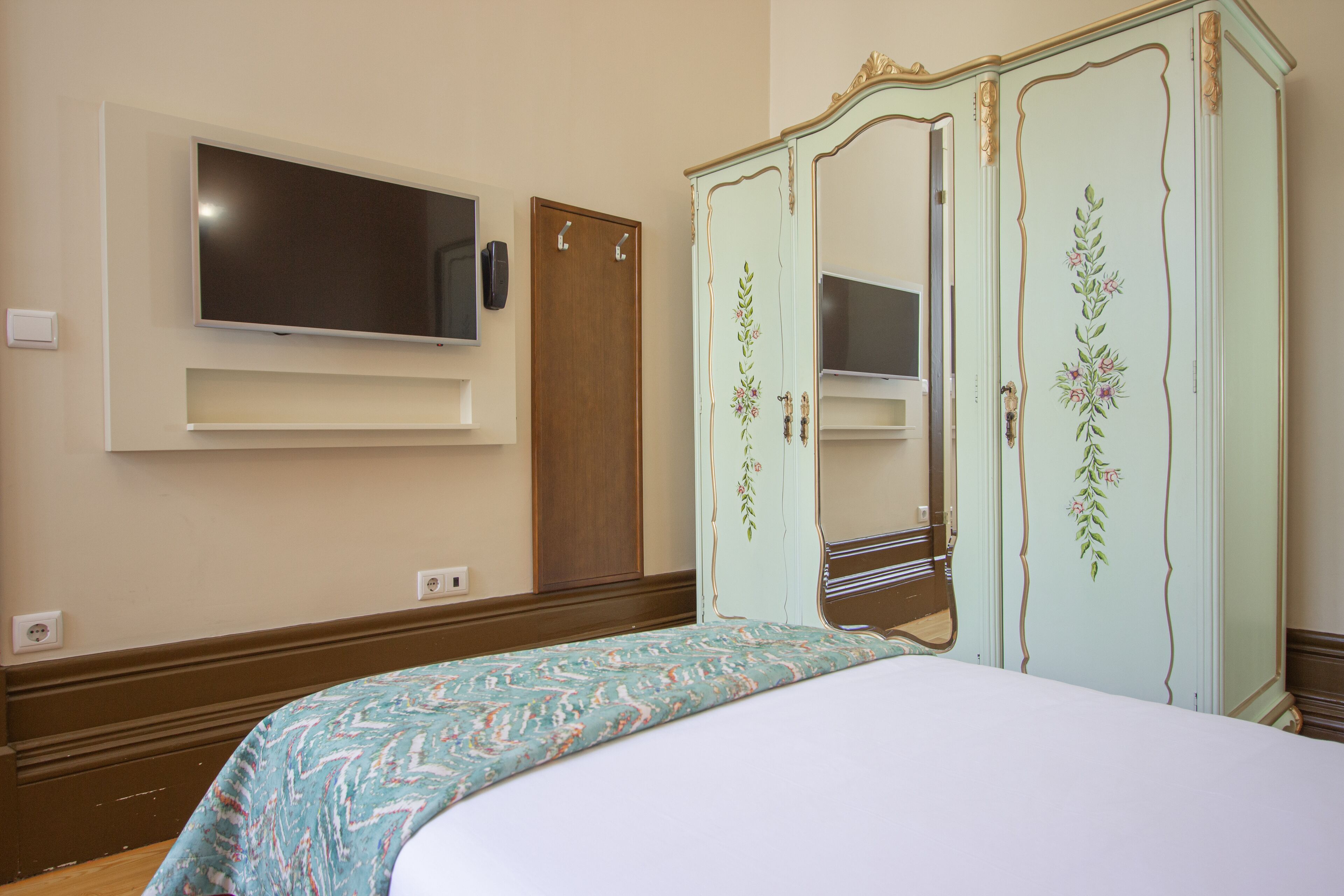 A bedroom with a bed, a television mounted on the wall, and a wardrobe with floral designs.