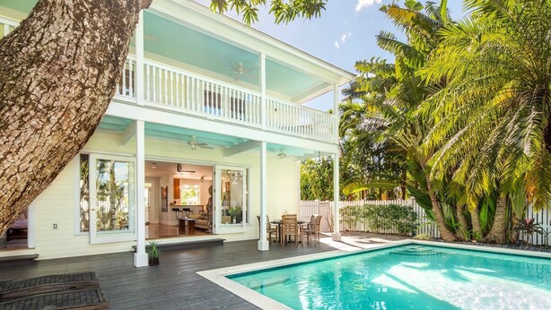 Una casa de dos pisos con piscina, balcón y vegetación tropical.