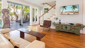 Un salón amplio con suelo de madera, un sillón de cuero marrón, un sofá blanco, una mesa de centro de madera y un aparador azul rústico.