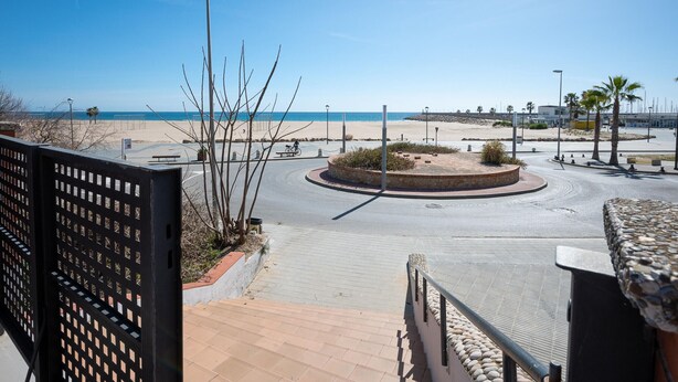 Blick auf eine Strandpromenade mit Kreisverkehr, Palmen und blauem Himmel.