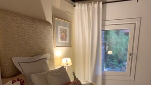 A neatly arranged bedroom with a bed, pillows, a bedside table with a lamp, and a window with curtains. - Small Luxury Apartment (Venezia)