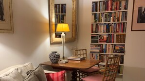 A cozy living room with a white sofa, a wooden dining table, a chair, a bookshelf, and a lamp. - Small Luxury Apartment (Venezia)