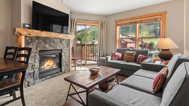A living room with a stone fireplace, a sofa, a table, and a TV mounted on the wall. - 1 Minute Walk to the Super Bee Chair! Enjoy the Best of Copper from this Beautif (Frisco)