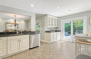 A kitchen with white cabinets, a stainless steel dishwasher, and a large window overlooking a garden. - New rental property, The Oasis (Kiawah Island)