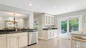 A kitchen with white cabinets, a stainless steel dishwasher, and a large window overlooking a garden. - New rental property, The Oasis (Kiawah Island)