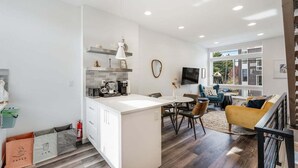 A modern kitchen with white cabinetry, a central island, and a dining area with a yellow sofa and chairs.