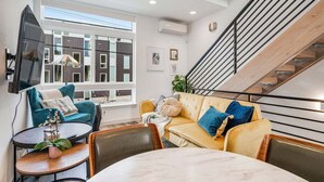 A modern living room with a sofa, chairs, a dining table, and a staircase.