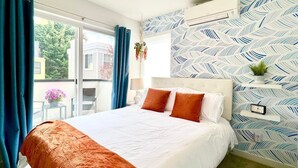 A hotel room with a large bed, a window with blue curtains, a patterned wall, and a small table with a plant.