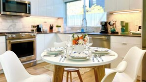 A modern kitchen with white cabinetry, a microwave, an oven, and a dining table set for four with plates, glasses, and cutlery.