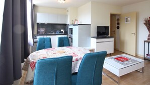 A modern kitchen with white cabinets, a black countertop, and a microwave. There is a dining area with a white table and blue chairs. - La Bourboule: T2 bis Apartment for 5 ppl, 49m², with Wifi (La Bourboule)
