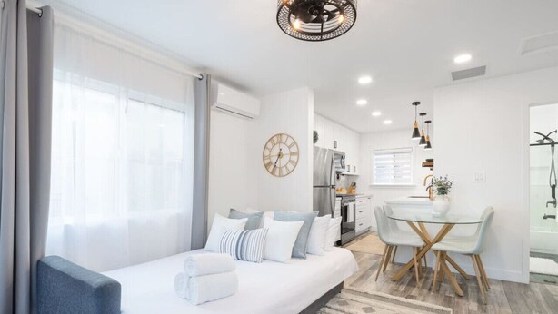 A modern hotel room with a bed, a small seating area, a dining table, and a kitchen in the background. - Charming 2BR Oasis w/ Fire Pit & BBQ, Downtown SD (San Diego)