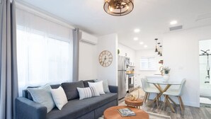 A modern living room with a grey sofa, a round coffee table, and a dining area with a glass table and wooden chairs. - Charming 2BR Oasis w/ Fire Pit & BBQ, Downtown SD (San Diego)