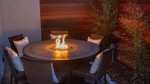 A round outdoor dining table with a built-in fire feature, surrounded by wicker chairs with cushions. - Charming 2BR Oasis w/ Fire Pit & BBQ, Downtown SD (San Diego)