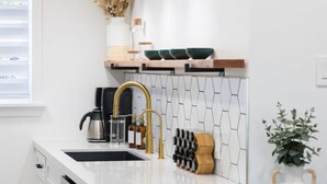 A modern kitchen with a white countertop, a gold faucet, and a black coffee maker. - Charming 2BR Oasis w/ Fire Pit & BBQ, Downtown SD (San Diego)