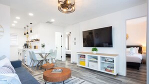 A modern living room with a sofa, coffee table, TV, and a bookshelf. - Charming 2BR Oasis w/ Fire Pit & BBQ, Downtown SD (San Diego)