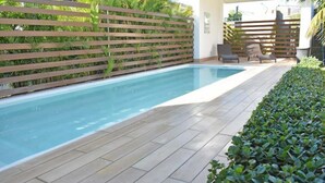 A rectangular pool with a wooden deck and a wooden fence with greenery behind it.